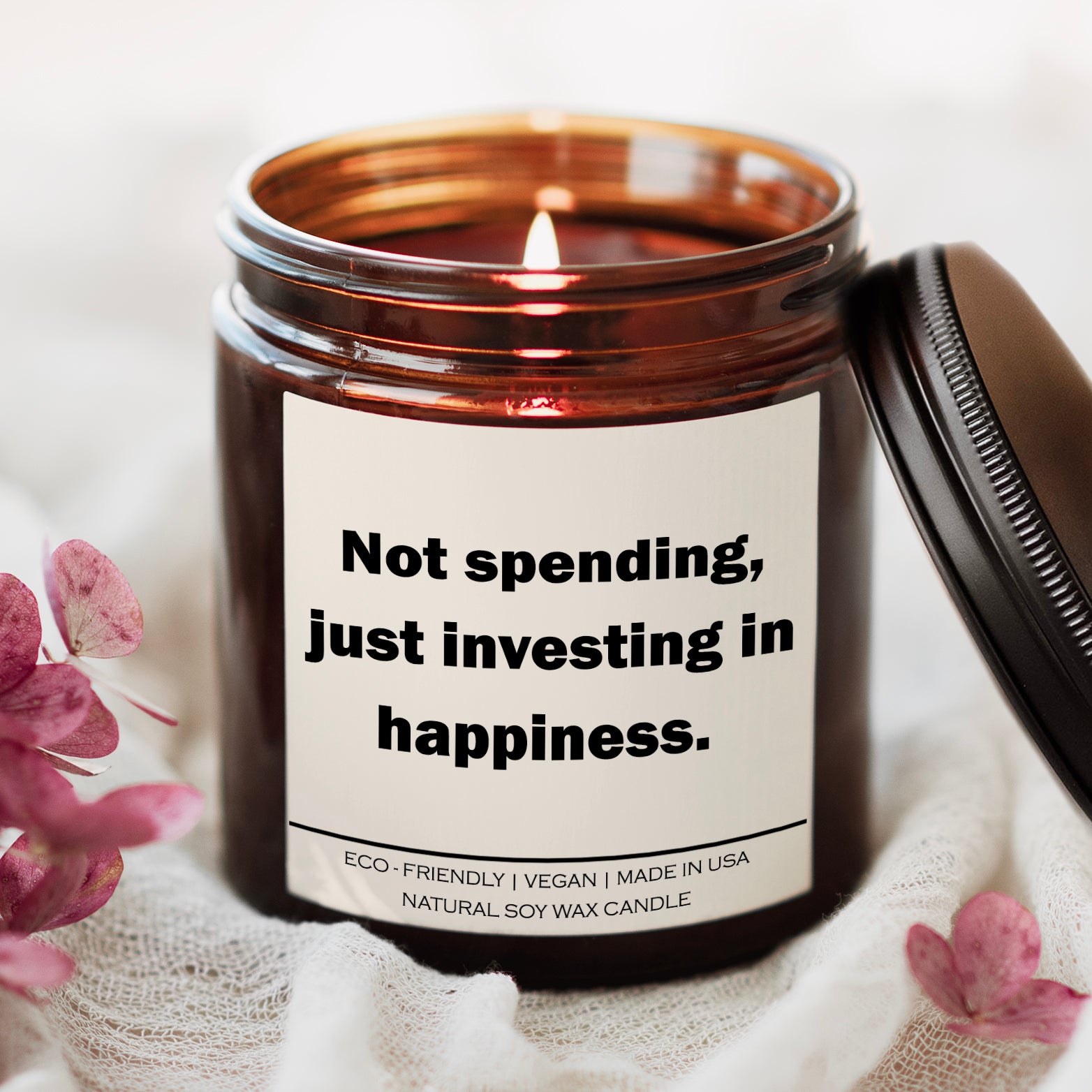 Eco-friendly soy wax candle with a label stating, "Not spending, just investing in happiness," surrounded by petals.
